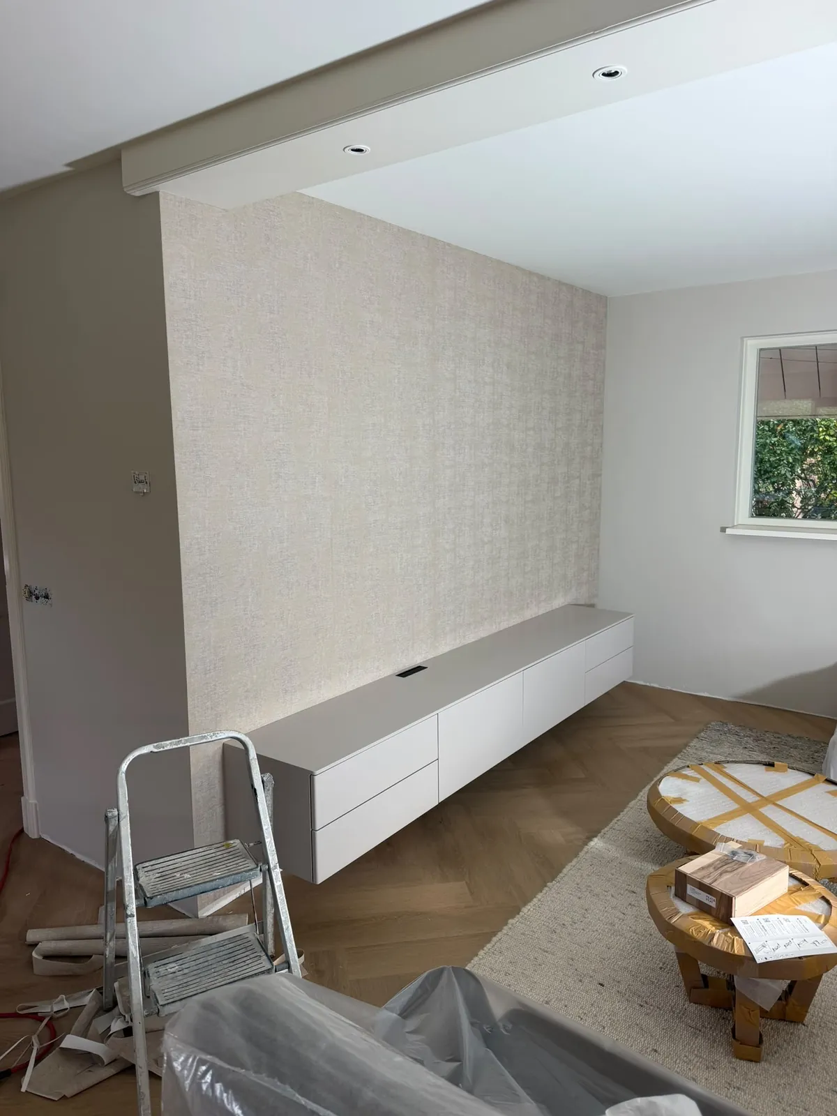 Pas behangen wand in een woonkamer, de trap en afdekfolie staan er nog