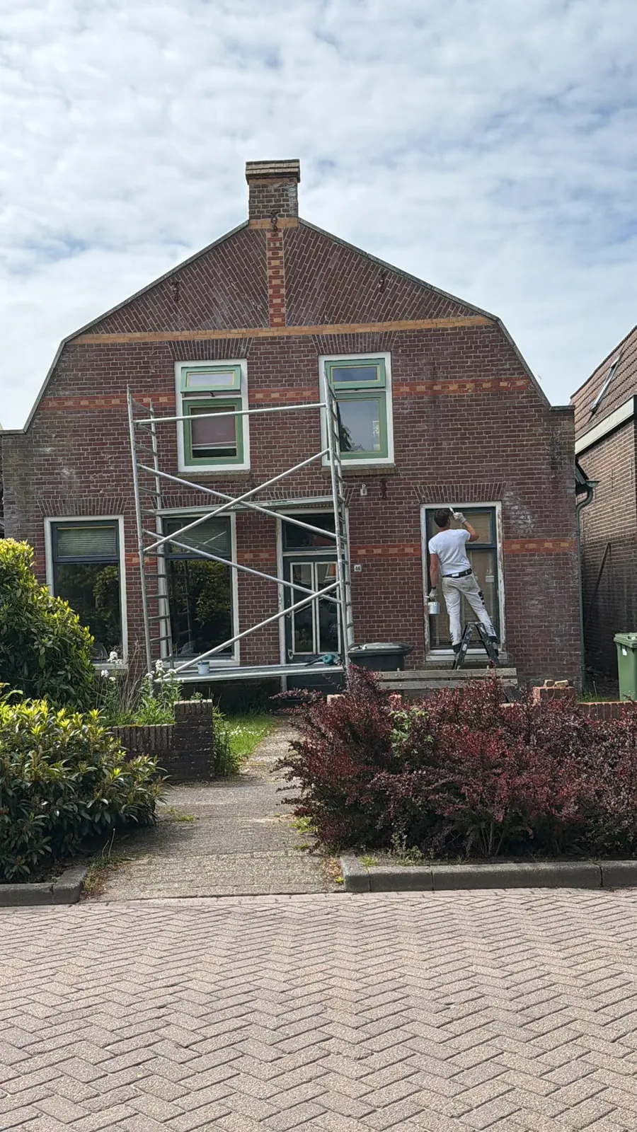 Bakstenen huis met steiger voor de gevel, een schilder werkt aan een raam