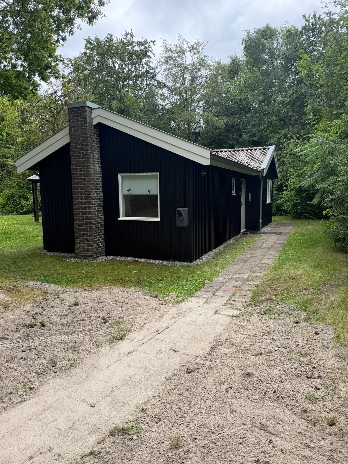 Zwart houten huisje tussen de bomen met witte kozijnen
