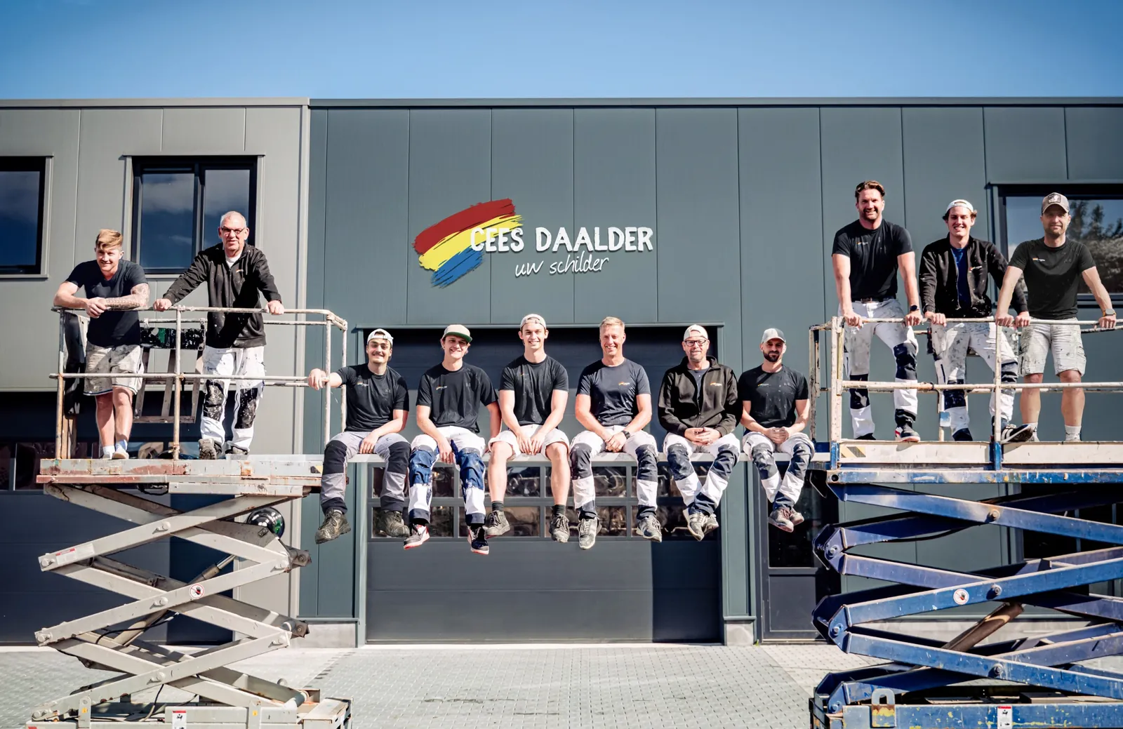 Het team van Schildersbedrijf Cees Daalder op twee hoogwerkers voor het bedrijfspand met logo